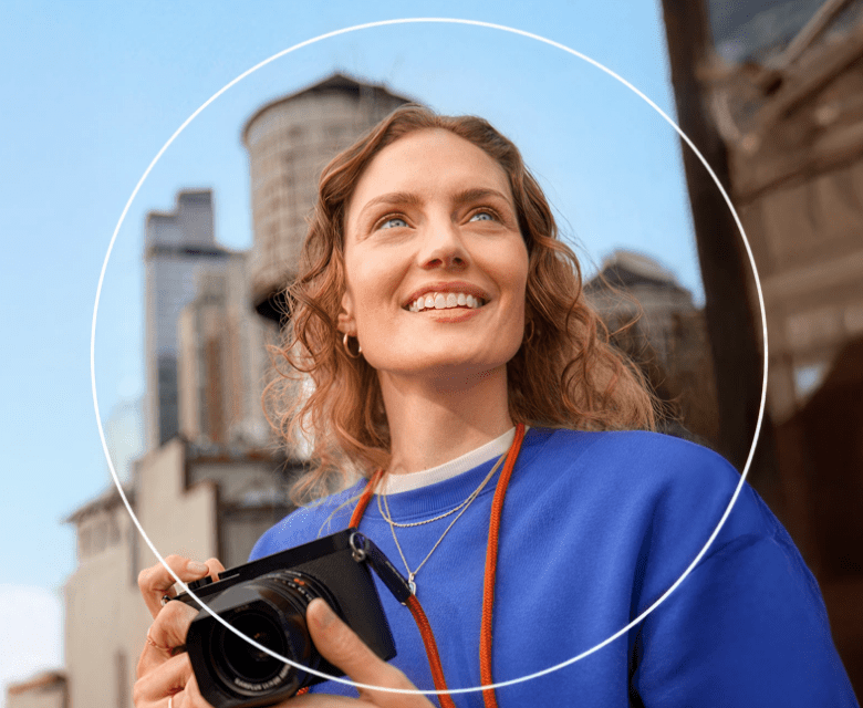 Woman outside holding a camera and looking off into the distance with a white circle around her.